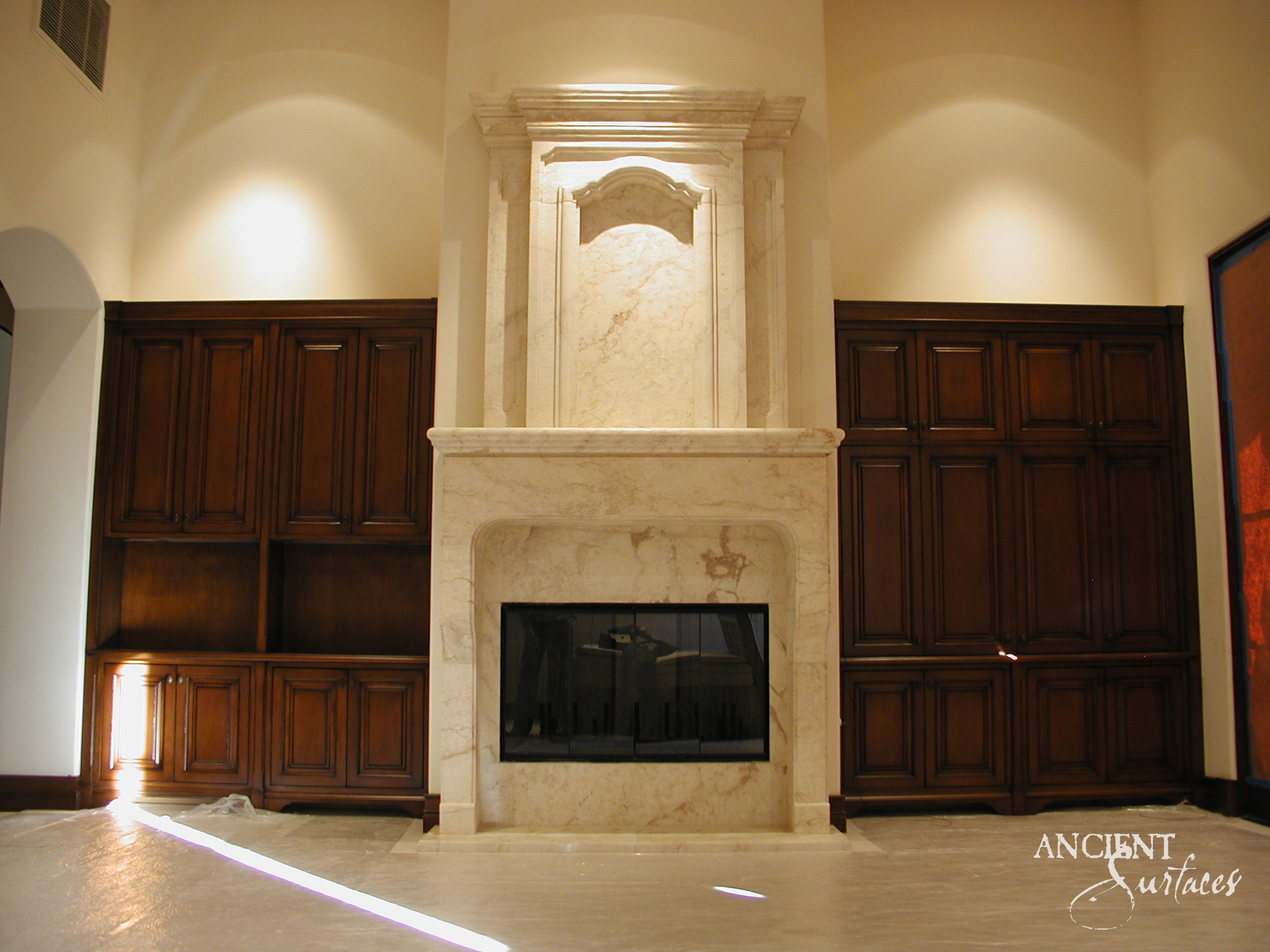 Full height reclaimed antique limestone chimneypiece from Ancient Surfaces with a carved arched overmantel between timber cabinetry