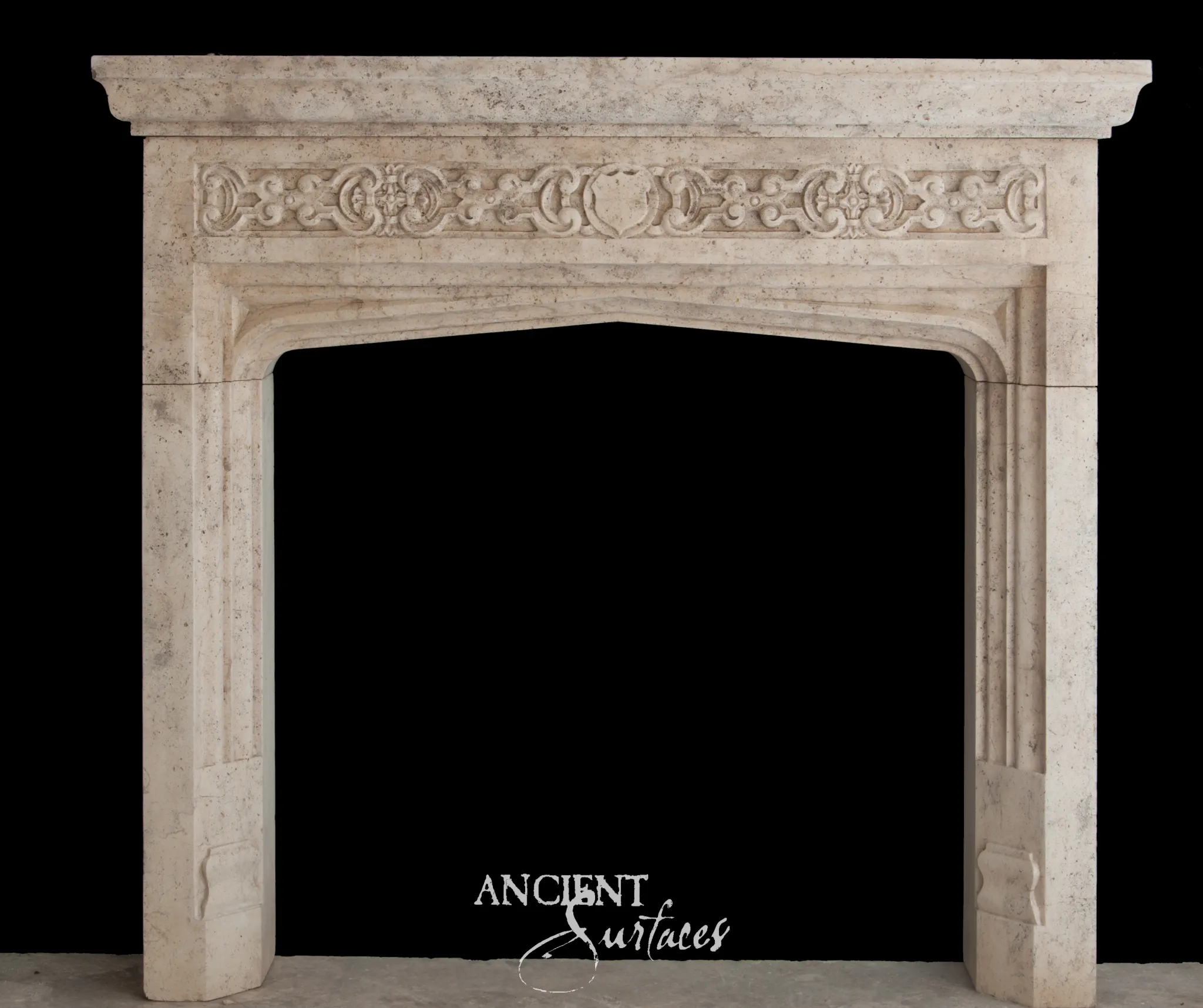 Reclaimed antique limestone fireplace mantel from Ancient Surfaces with a Tudor arch opening and carved interlace frieze
